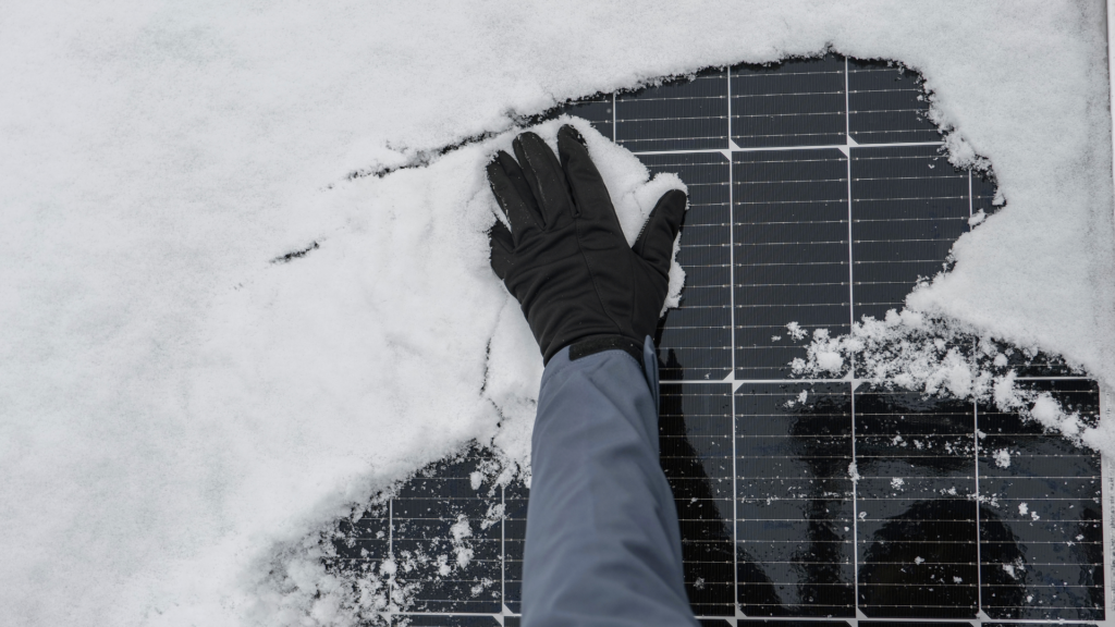 Un technicien nettoie des panneaux solaires recouverts de neige, illustrant leur fonctionnement par mauvais temps.